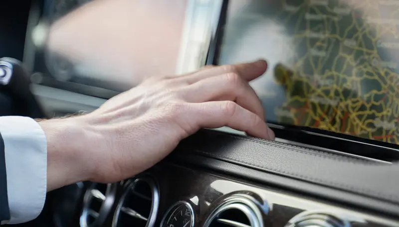 Mão do condutor junto ao ecrã de navegação no tablier de um carro